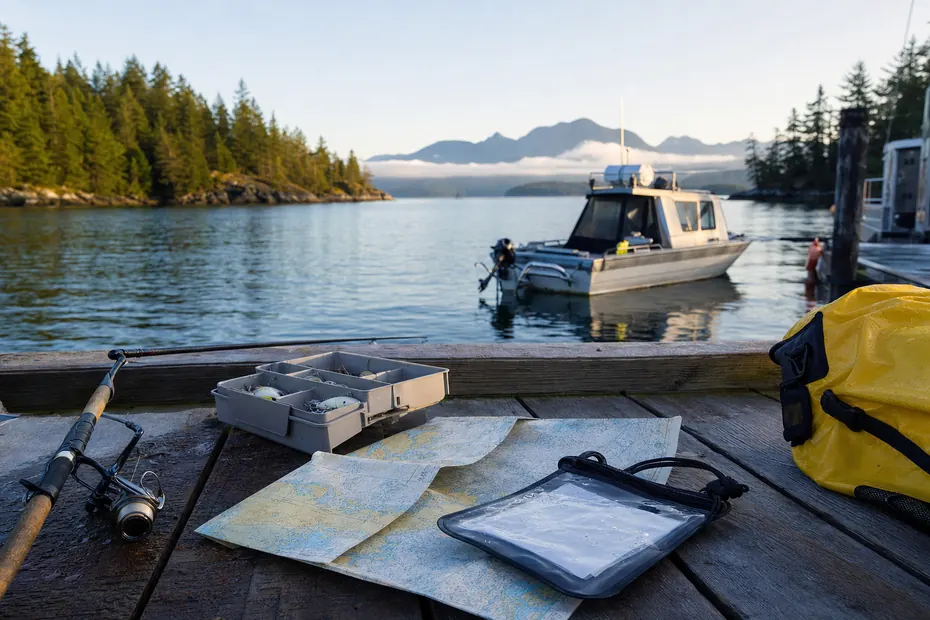 BC tidal-water fishing licence planning with rod tackle nautical chart waterproof document pouch and boat at a Pacific coastal dock